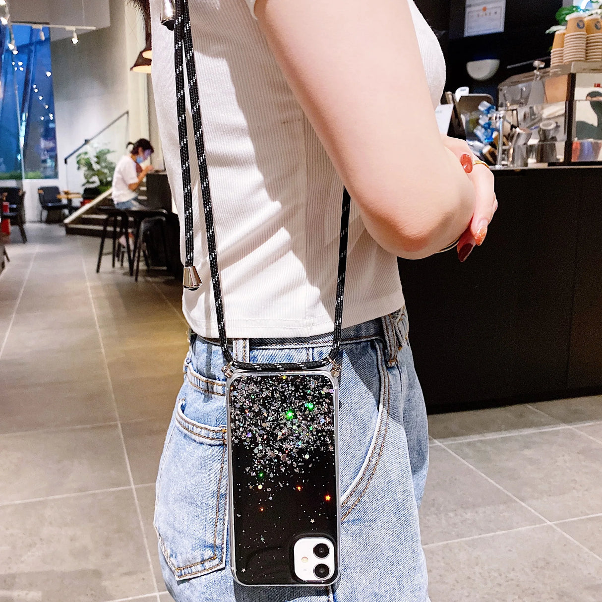 A glittery black iPhone case with a black and white crossbody strap.