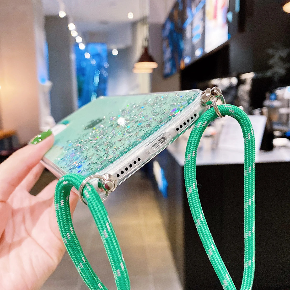 A clear phone case filled with green glitter and attached to a green braided lanyard.