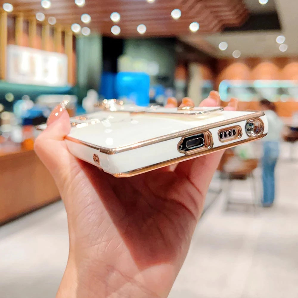 A hand holding a white smartphone case with gold edges and a kickstand.