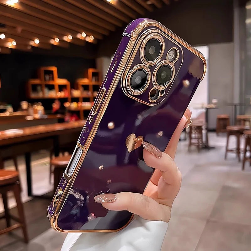 A person holding a purple smartphone with a gold-trimmed case, decorative studs, and a heart-shaped charm.