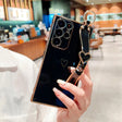 Black smartphone with a gold-trimmed case, a heart-shaped design, and a black and gold heart-shaped wrist strap.