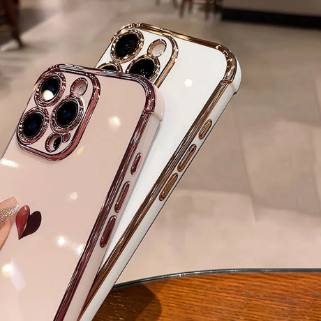 Two shiny phone cases, one pink and one white, both with gold-colored edges and camera protection.