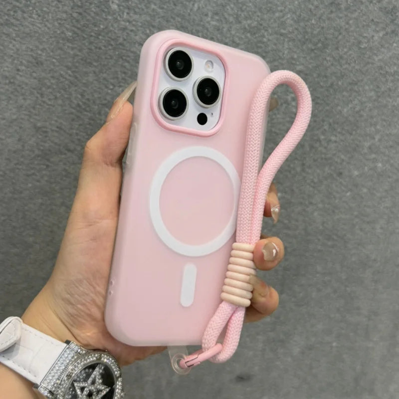 Pink iPhone case with a circular MagSafe ring, integrated camera lens protection, and an attached pink braided wrist strap with a beige coiled accent.