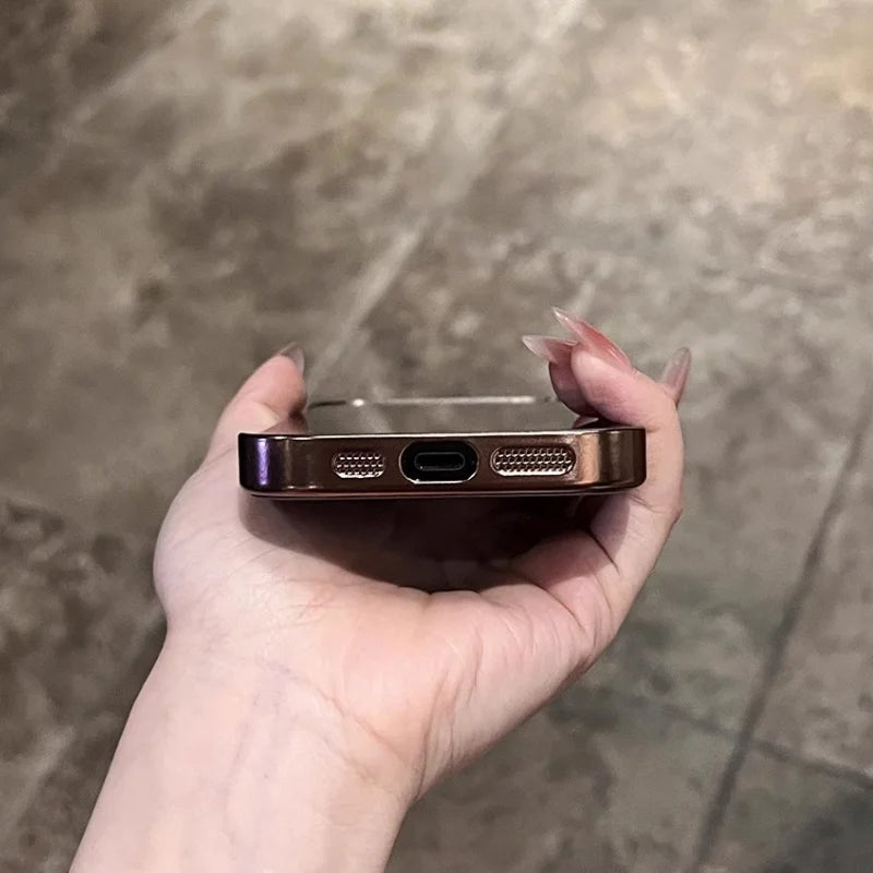 A hand holding a rose gold smartphone with a charging port and speaker grilles visible on the bottom edge.
