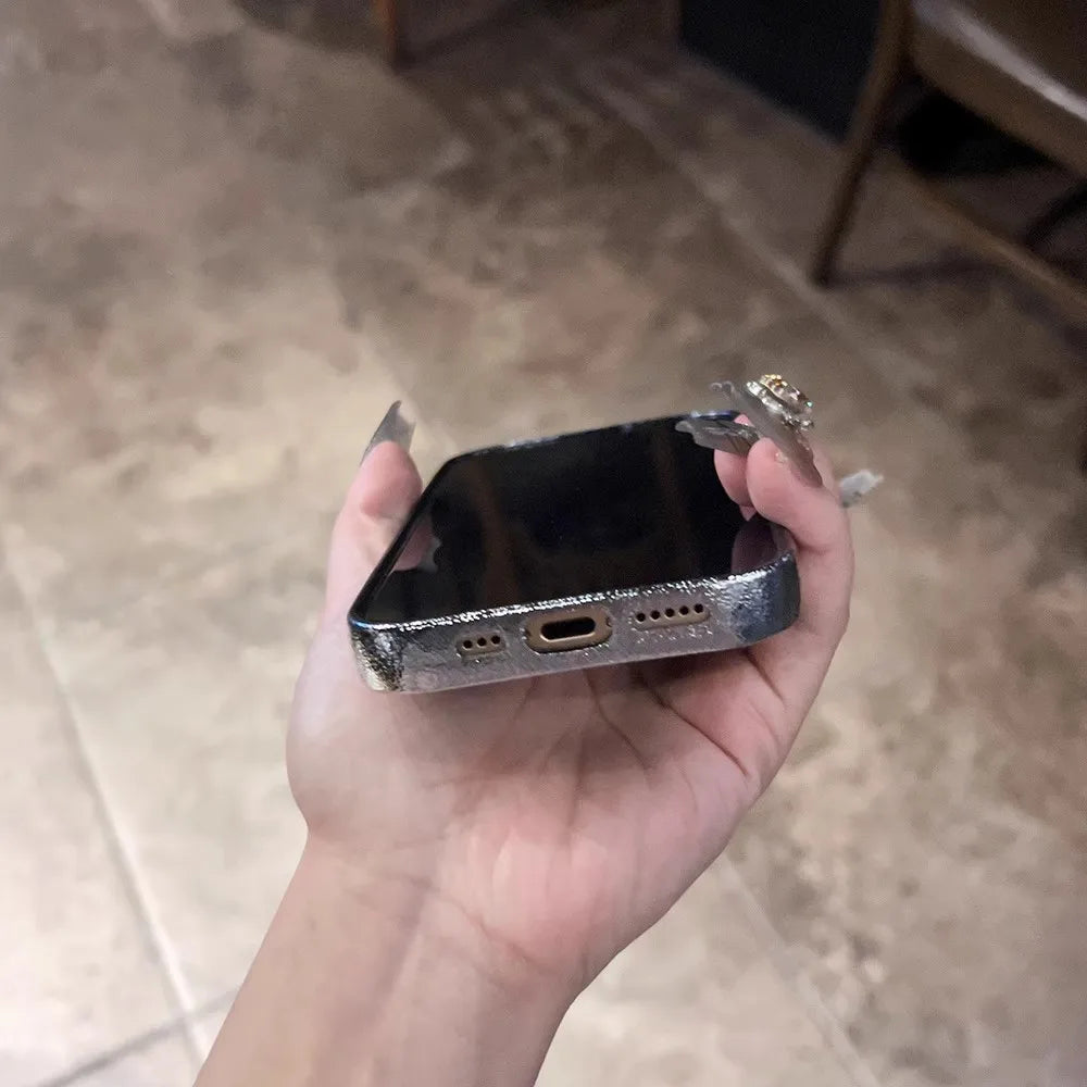 A hand holding a silver-colored smartphone with a charging port and speaker grilles visible on the bottom edge.