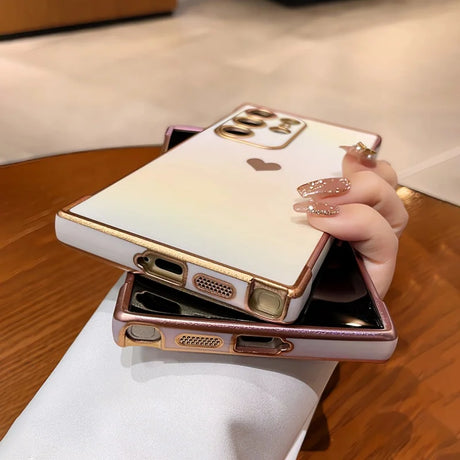 Two gradient-colored phone cases with gold trim and a heart-shaped cutout, one held by a hand with glittery nails.