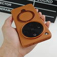 Brown leatherette phone case with an integrated ring holder and a prominent circular camera cutout.