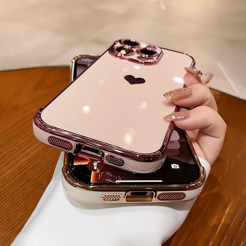 A shiny, pink iPhone case with a black heart design, a jeweled camera outline, and a metallic rose gold bumper.
