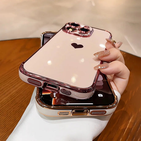 A shiny, pink iPhone case with a black heart design, a jeweled camera outline, and a metallic rose gold bumper.