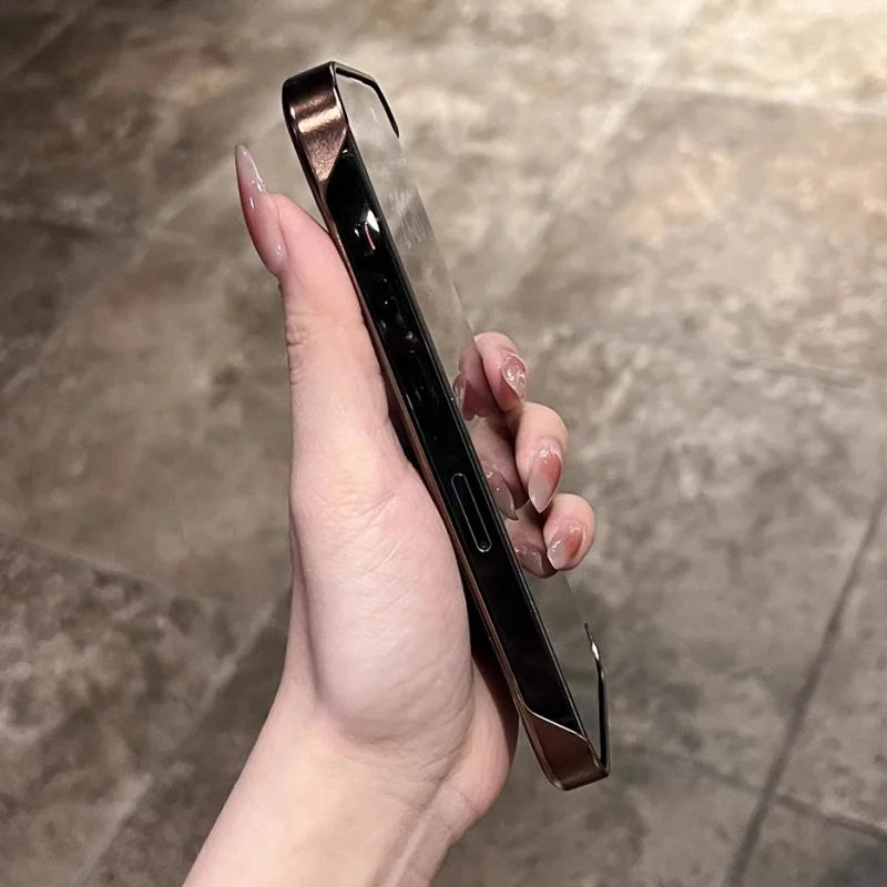 A hand holding a smartphone with a metallic, possibly bronzed, bumper case that has a clear back.