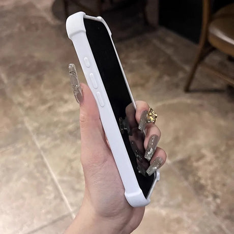 A white phone case protecting a smartphone, held by a hand with long, decorated nails and a gold ring.