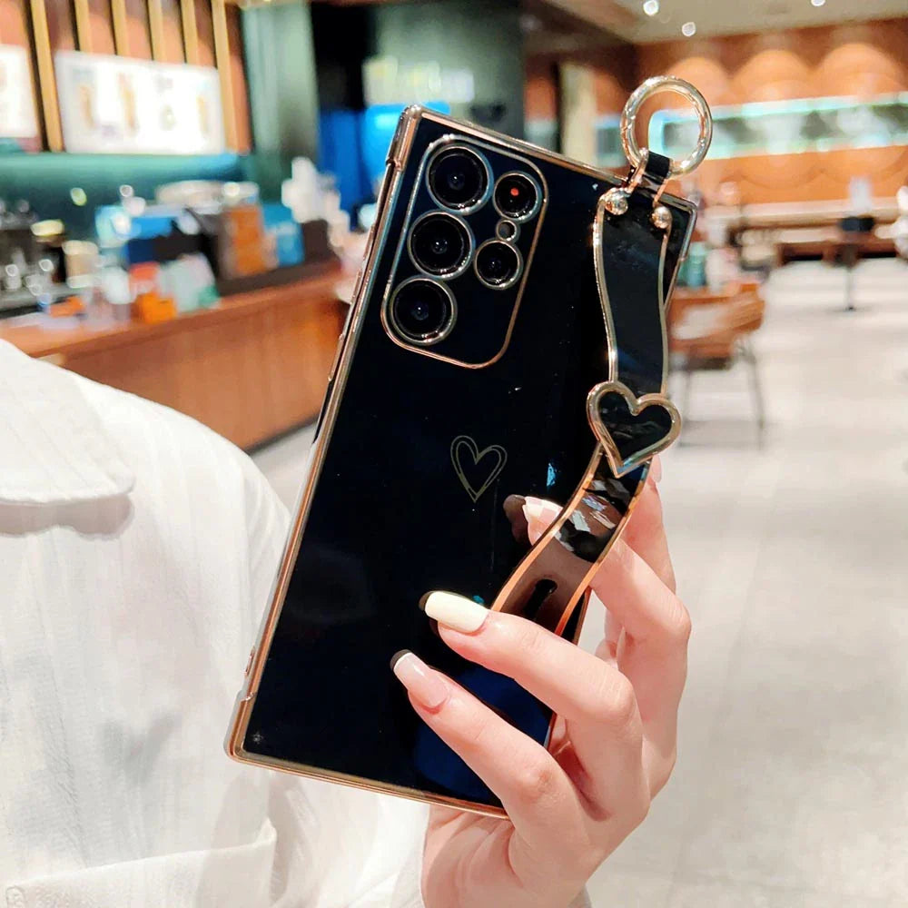 Black smartphone in a gold-edged case with a heart-shaped wrist strap.