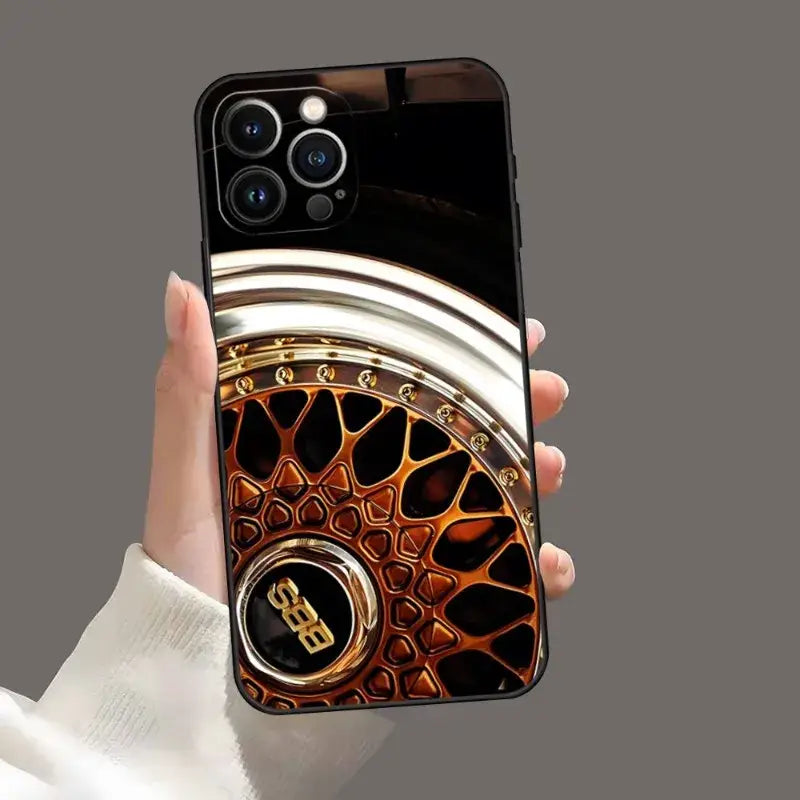 A hand holding a phone case with a gold and black design