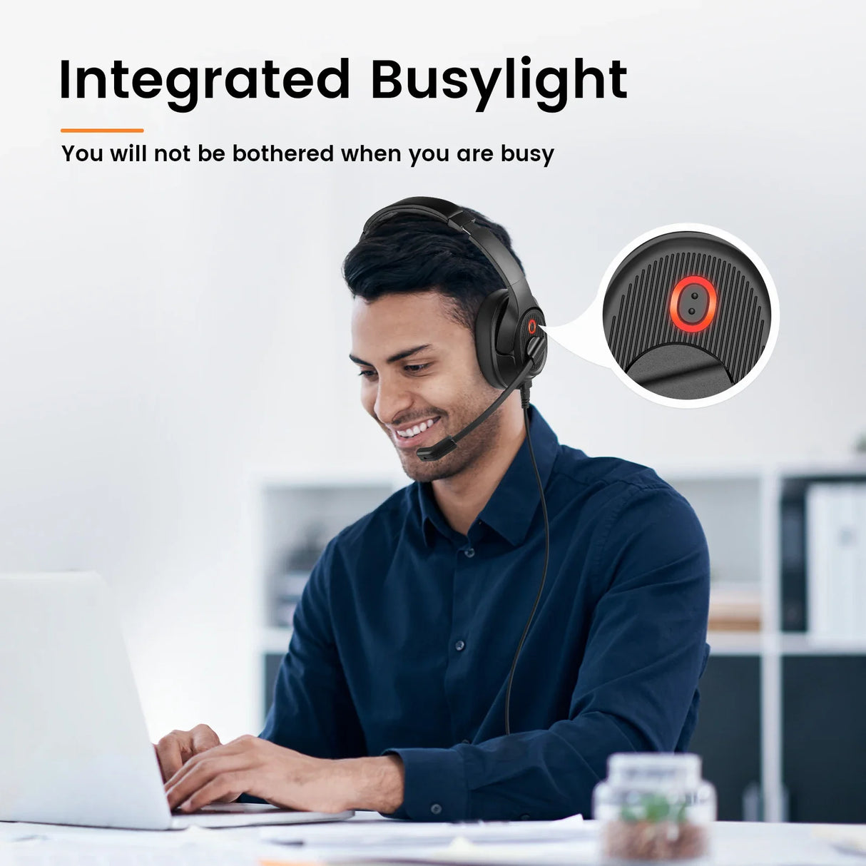 Headset with an integrated ’busylight’ feature worn by a smiling person working at a computer.
