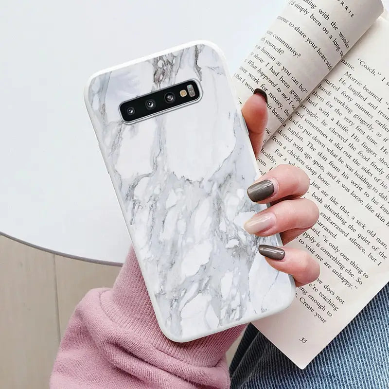 a woman holding a book and a white marble phone case