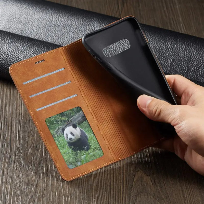 a hand holding a leather wallet with a panda face on it