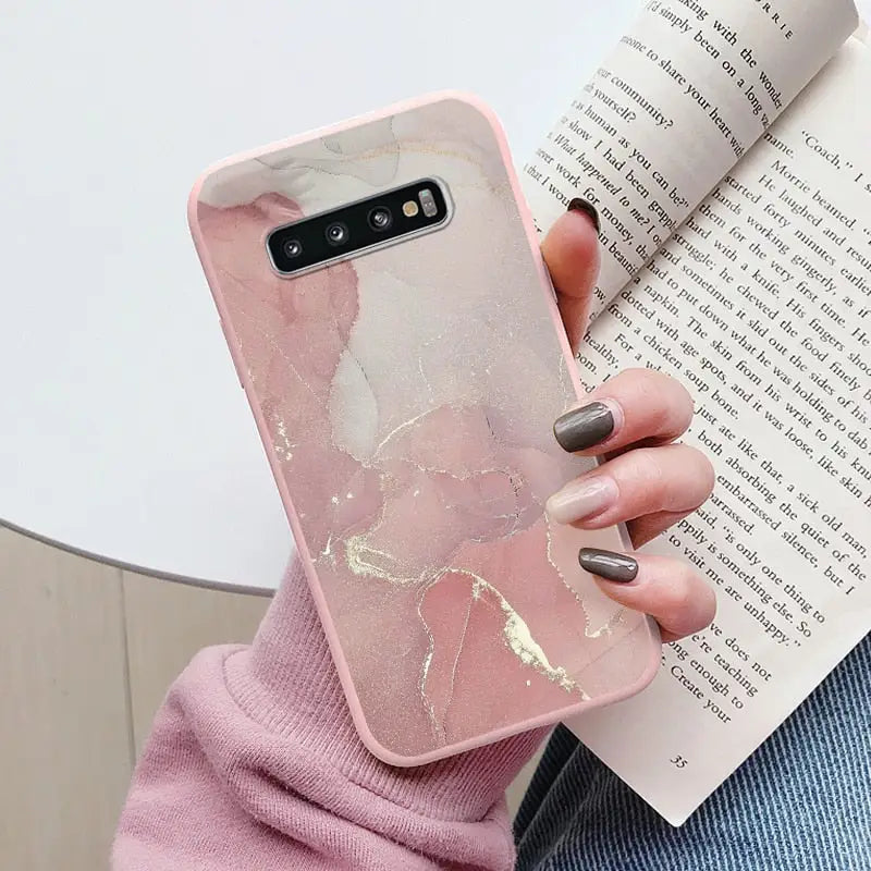 a woman holding a book and a pink marble phone case