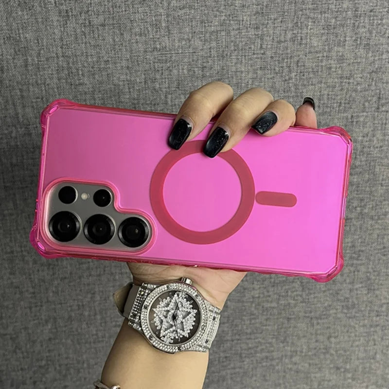 A hot pink smartphone with a clear case and a magnetic charging ring, held by a hand wearing a diamond-studded watch.