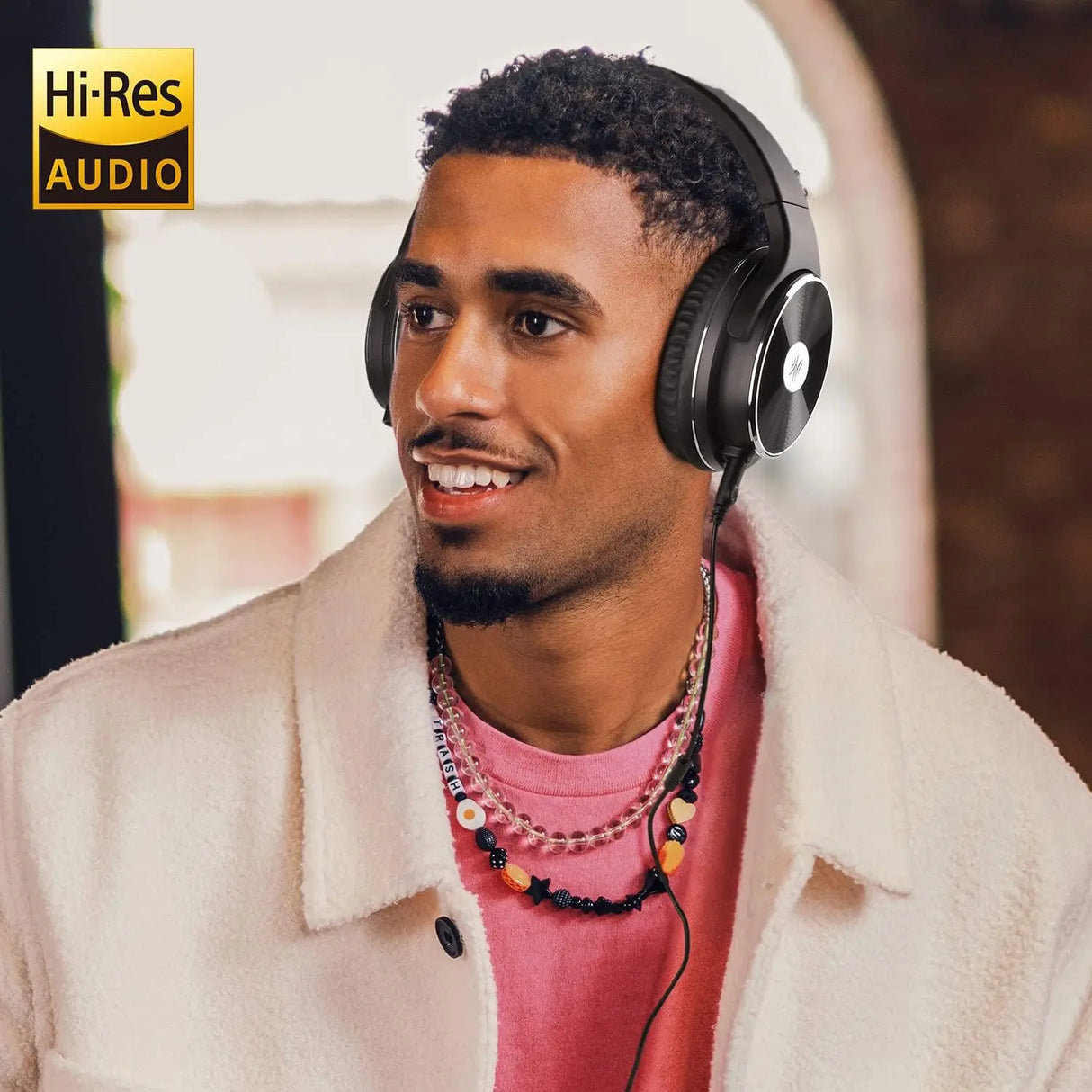 Man wearing headphones and a light-colored jacket over a pink shirt.