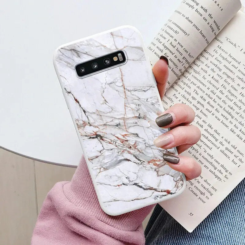 a woman holding a book and a white marble phone case