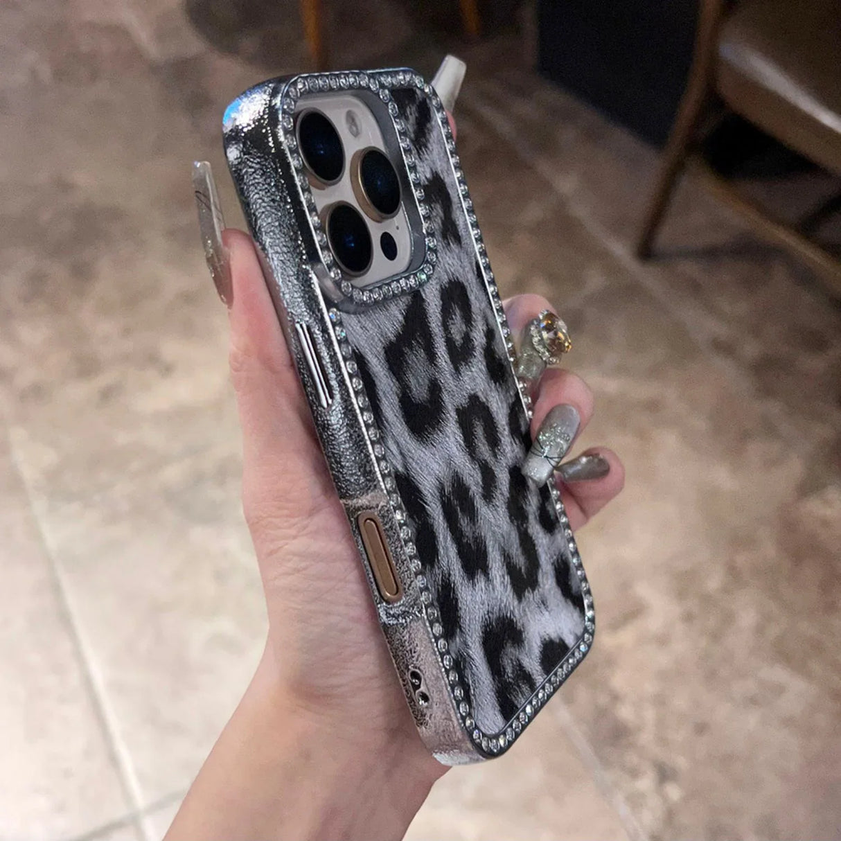 A silver and black leopard print iPhone case with rhinestone embellishments and a butterfly charm.