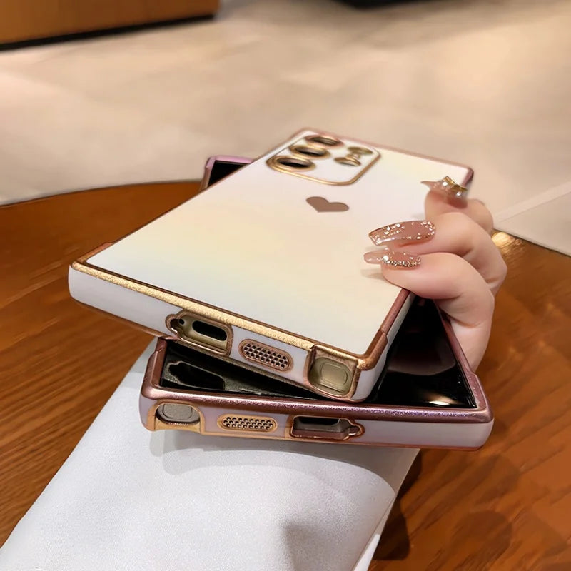 Two gradient-colored phone cases with gold trim and a heart-shaped cutout, one held by a hand with glittery nails.