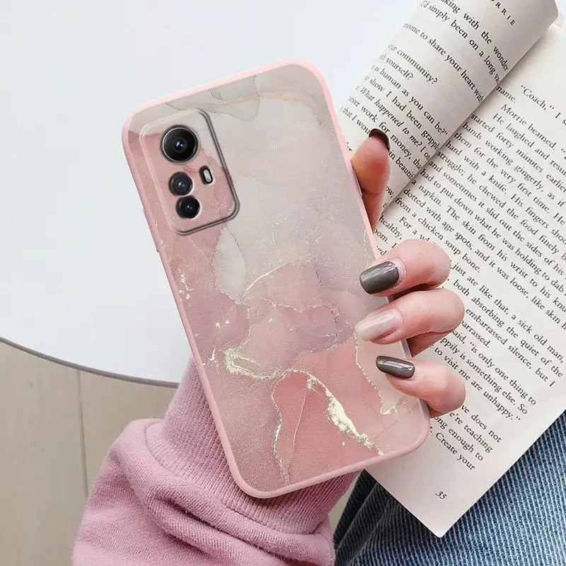 A woman holding a book and a pink marble phone case