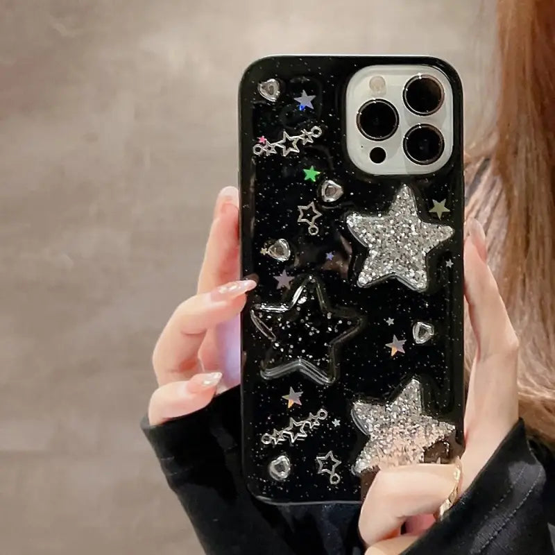 a woman holding a black phone case with stars and glitters