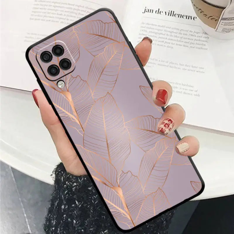 a woman holding a phone case with a gold leaf pattern