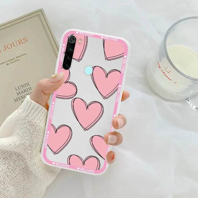 a woman holding a pink phone case with hearts on it