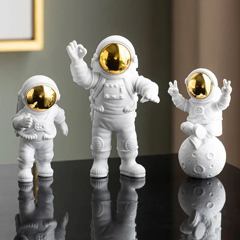 three small white and gold astronaut figuris on a table