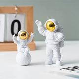 two small white and gold astronaut figuris on a table