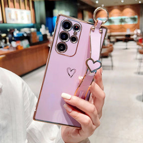Purple smartphone with a gold-trimmed case and a heart-shaped wrist strap.