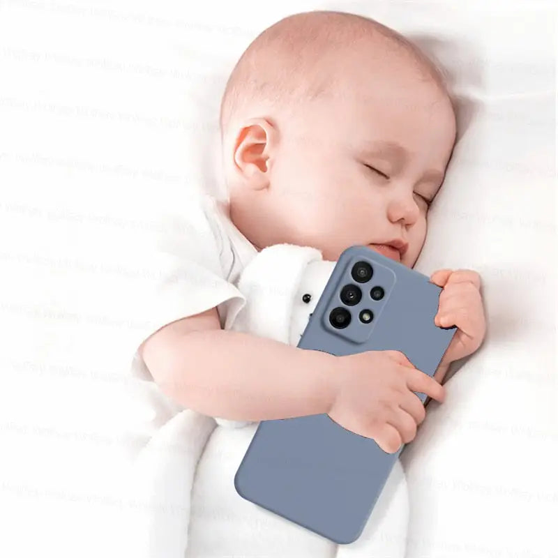 a baby sleeping on a white blanket holding a phone