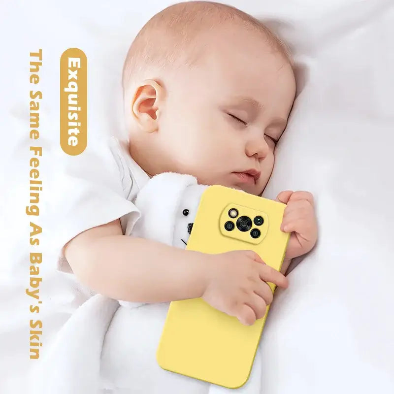 a baby sleeping on a white bed with a yellow phone case