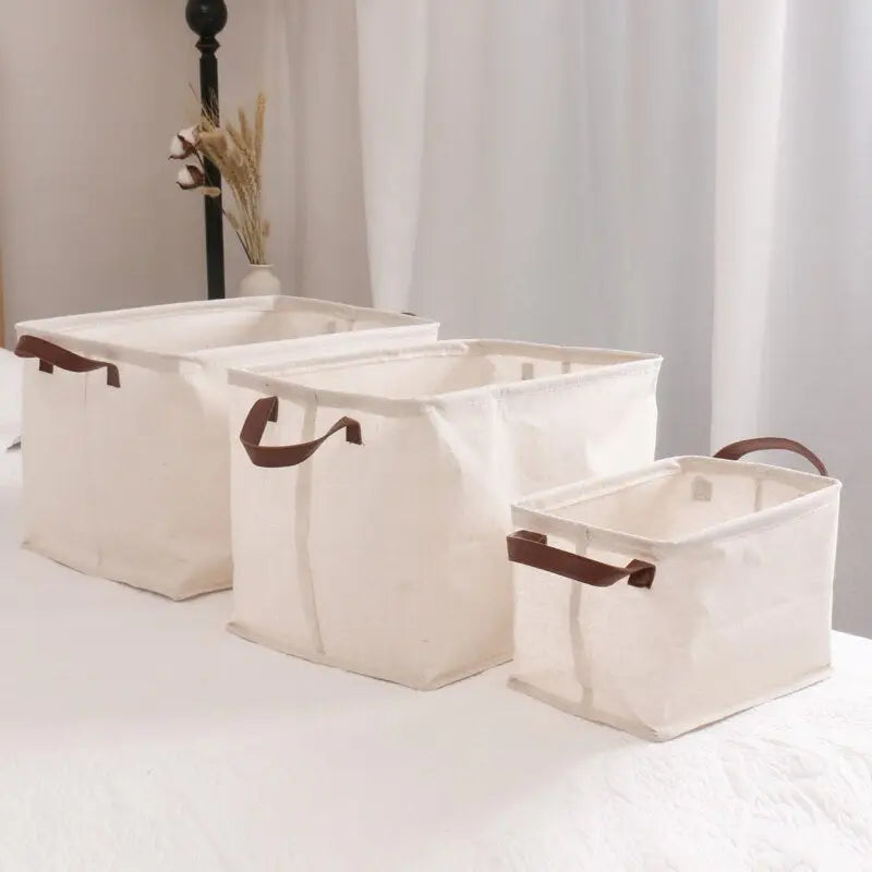 three white canvas storage baskets with brown leather handles