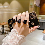 Black iPhone case with heart-shaped charms and decorative rings attached.