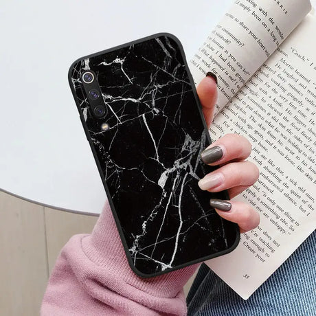 a woman holding a book and a black marble phone case