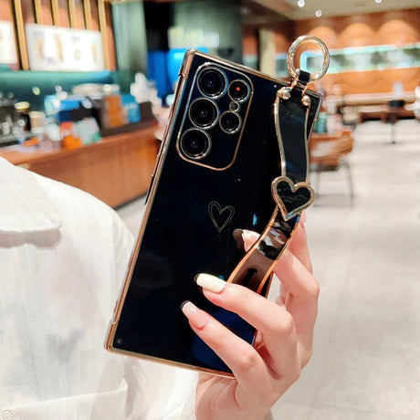 Black smartphone in a gold-edged case with a heart-shaped wrist strap.