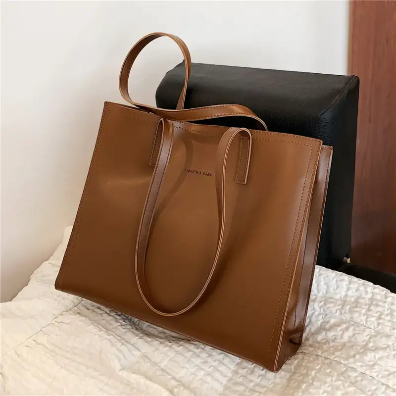 a brown leather tote bag on a bed