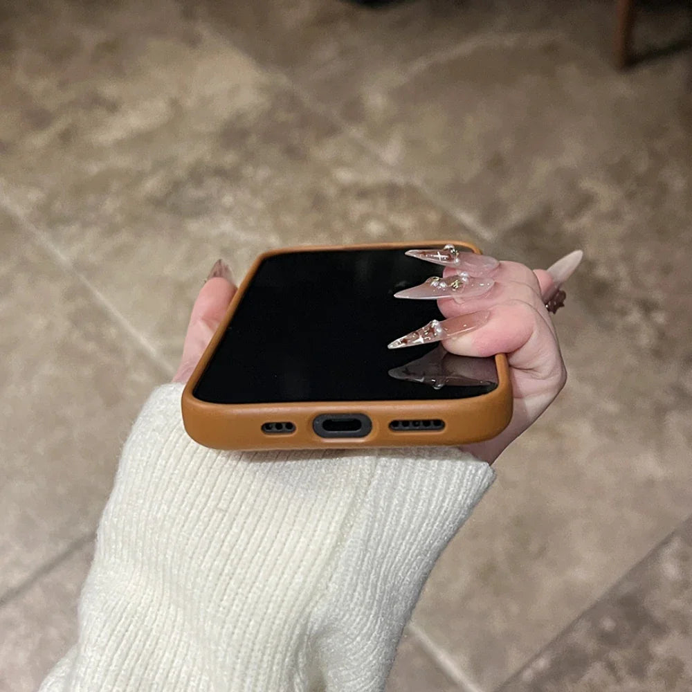 A brown phone case on a smartphone, held by a hand with long, clear, pointed nails.