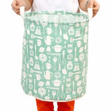 a child holding a large green bag with a pattern of kitchen items