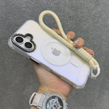 A clear iPhone case with a beige wrist strap, a black camera accent, and an Apple MagSafe charger.