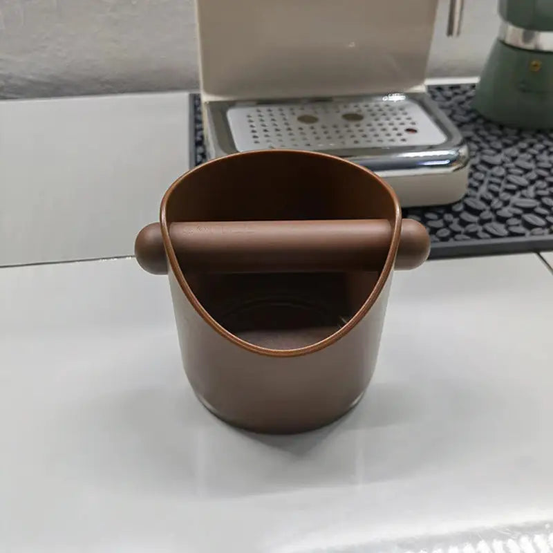 a cup on a table with a coffee maker in the background
