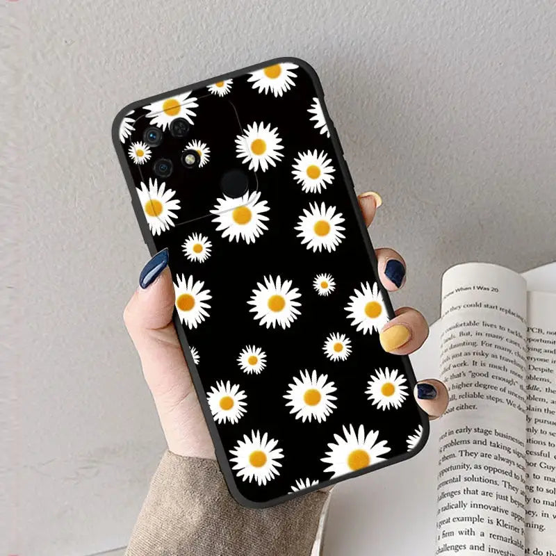 a woman holding a book and a phone case with daisies on it