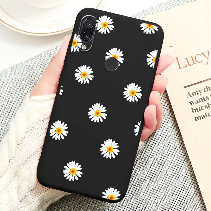 a person holding a black phone case with white daisies on it