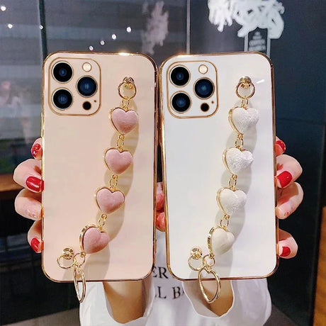 Decorative iPhone cases with heart-shaped charm straps in pink and white colors.