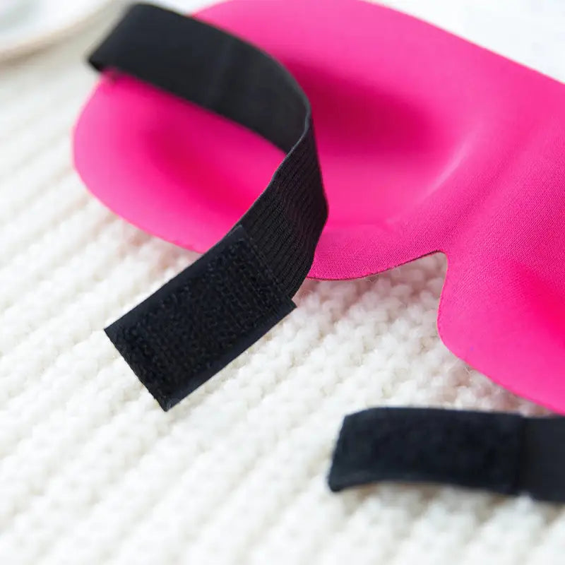 a pair of pink and black eye masks on a white blanket