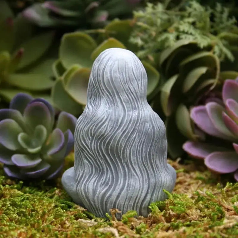 a small statue of a woman sitting on a moss covered ground