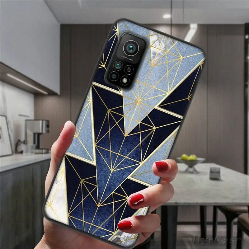 a woman holding a phone case with a gold geometric design